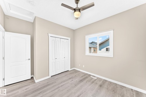 Expansive room featuring wood-finish flooring, a window with white trim, a ceiling fan with integrated lighting, and bi-fold closet doors - 16227 64 Street Nw, Edmonton, AB - Indoor Photo Showing Other Room