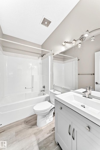 White vanity with a single basin sink, chrome faucet, and mirrored wall - 16227 64 Street Nw, Edmonton, AB - Indoor Photo Showing Bathroom