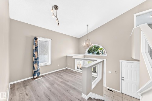 Vaulted ceiling with an arched window, wood-finish flooring, white paneled interior door, and a chandelier - 16227 64 Street Nw, Edmonton, AB - Indoor Photo Showing Other Room