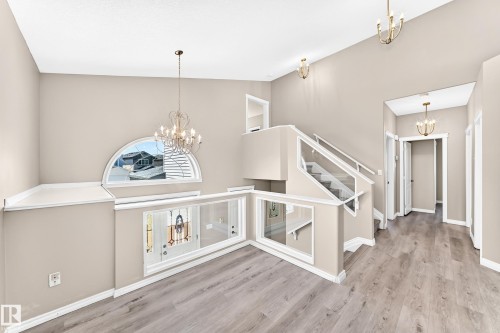 Vaulted ceilings, wood-finish flooring, glass panel staircase railing, arched window, and chandelier lighting - 16227 64 Street Nw, Edmonton, AB - Indoor Photo Showing Other Room