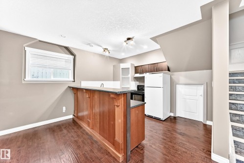 Wood-finish flooring with a multi-tone stain, kitchen with wood cabinetry, and a peninsula countertop with a built-in sink - 16227 64 Street Nw, Edmonton, AB - Indoor Photo Showing Kitchen