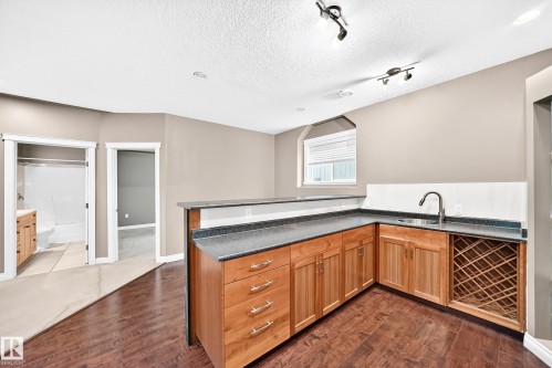 Wet bar featuring wood-finish cabinetry, dark countertops, built-in wine storage, and a stainless steel sink with a gooseneck faucet - 16227 64 Street Nw, Edmonton, AB - Indoor