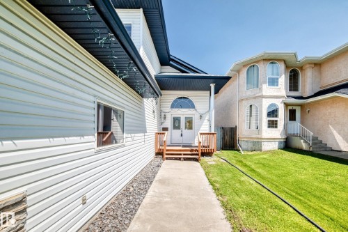 Light-colored horizontal siding, arched transom window above double entry doors, wood-finish porch railing, concrete walkway, and dark gravel landscaping - 16227 64 Street Nw, Edmonton, AB - Outdoor