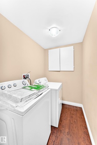 Dedicated laundry area featuring a washer and dryer, wood-finish flooring, and wall-mounted cabinetry - 16227 64 Street Nw, Edmonton, AB - Indoor Photo Showing Laundry Room