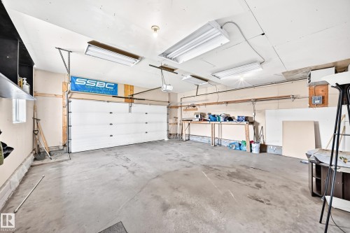 Concrete floor, white paneled garage door, exposed ceiling joists, fluorescent lighting fixtures, and a wall-mounted workbench - 16227 64 Street Nw, Edmonton, AB - Indoor Photo Showing Garage