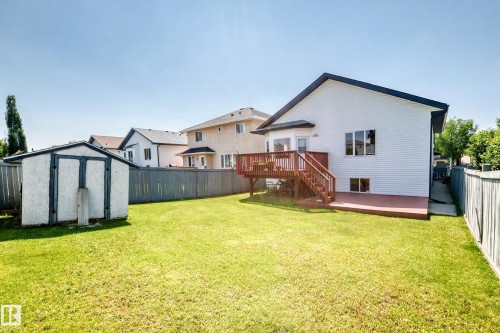 Expansive green lawn, elevated wood deck, lower ground-level deck, white siding exterior, and a detached storage shed - 16227 64 Street Nw, Edmonton, AB - Outdoor With Backyard With Exterior