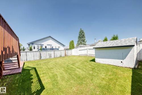 Expansive lawn with a wood deck, wood privacy fencing, and a detached storage shed with an asphalt shingle roof - 16227 64 Street Nw, Edmonton, AB - Outdoor With Deck Patio Veranda