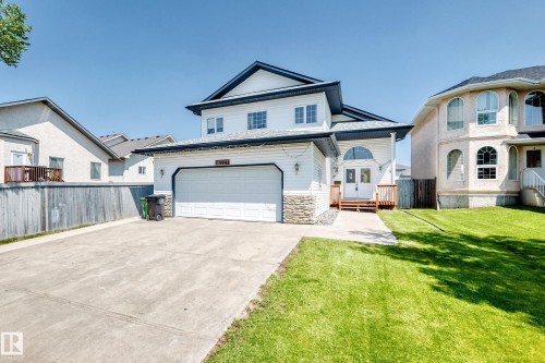 Two-story exterior with white siding and dark trim, featuring a double garage, concrete driveway, and stone accent detailing - 16227 64 Street Nw, Edmonton, AB - Outdoor With Facade