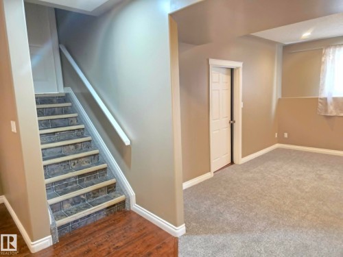 Staircase with tile treads and a white handrail, wood-finish flooring, and carpeted room with a window - 16227 64 Street Nw, Edmonton, AB - Indoor Photo Showing Other Room
