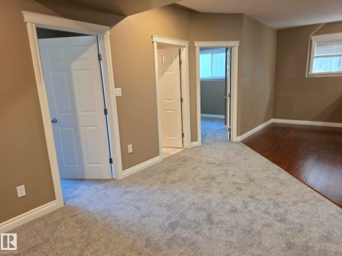 Plush grey carpeting complemented by rich wood-finish flooring - 16227 64 Street Nw, Edmonton, AB - Indoor Photo Showing Other Room