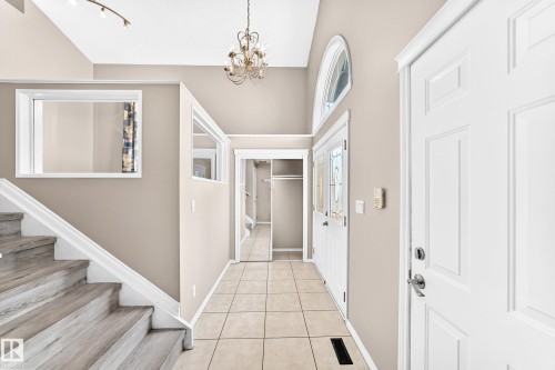 Vaulted ceiling with an ornate chandelier, wood-finish stairs, main entry door with decorative glass, and tiled flooring - 16227 64 Street Nw, Edmonton, AB - Indoor Photo Showing Other Room