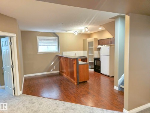 Compact kitchen area featuring wood-finish flooring, a built-in island with a sink, and dark wood cabinetry - 16227 64 Street Nw, Edmonton, AB - Indoor Photo Showing Kitchen