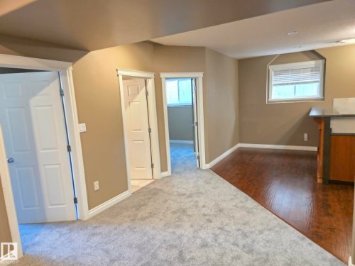 Neutral tone wall paint, light gray carpeting, wood-finish flooring, white paneled doors, and a built-in counter with cabinetry - 16227 64 Street Nw, Edmonton, AB - Indoor Photo Showing Other Room