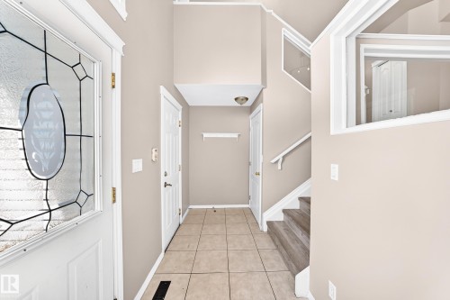Foyer featuring a leaded glass entry door, tile flooring, wood-finish staircase, and a high ceiling - 16227 64 Street Nw, Edmonton, AB - Indoor Photo Showing Other Room