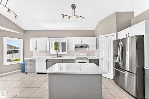 Kitchen featuring an island with a quartz countertop, white upper cabinetry, gray lower cabinetry, and stainless steel appliances - 16227 64 Street Nw, Edmonton, AB - Indoor Photo Showing Kitchen With Upgraded Kitchen