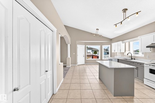 Vaulted ceiling, track lighting, kitchen island with solid surface countertop, tile flooring, and white cabinetry - 16227 64 Street Nw, Edmonton, AB - Indoor Photo Showing Kitchen