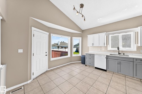 Spacious kitchen featuring gray cabinetry, stainless steel appliances including a dishwasher and range, tile flooring, and abundant natural light from multiple windows - 16227 64 Street Nw, Edmonton, AB - Indoor Photo Showing Kitchen