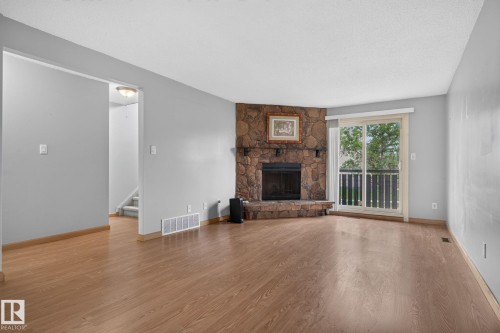 Living area featuring wood-finish flooring, a corner stone fireplace, and a sliding glass door providing exterior access - 10644 158 Avenue Nw, Edmonton, AB - Indoor Photo Showing Living Room With Fireplace