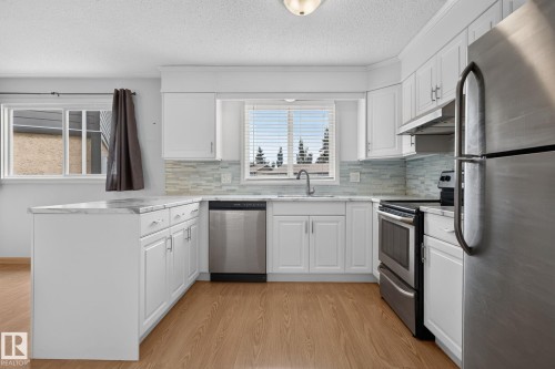 Kitchen featuring white cabinetry, light-toned wood-finish flooring, stainless steel appliances, a mosaic tile backsplash, and a corner sink with a window - 10644 158 Avenue Nw, Edmonton, AB - Indoor Photo Showing Kitchen With Stainless Steel Kitchen With Upgraded Kitchen