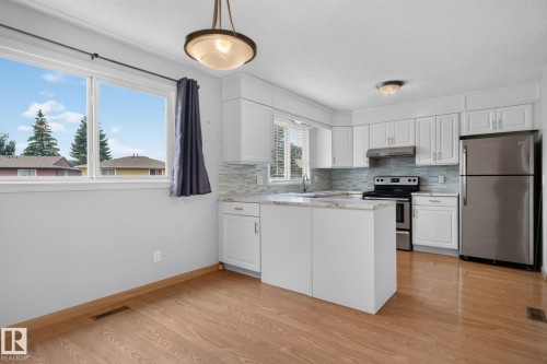 Kitchen featuring white cabinetry, light-colored countertops, stainless steel appliances, and a tiled backsplash - 10644 158 Avenue Nw, Edmonton, AB - Indoor Photo Showing Kitchen With Stainless Steel Kitchen