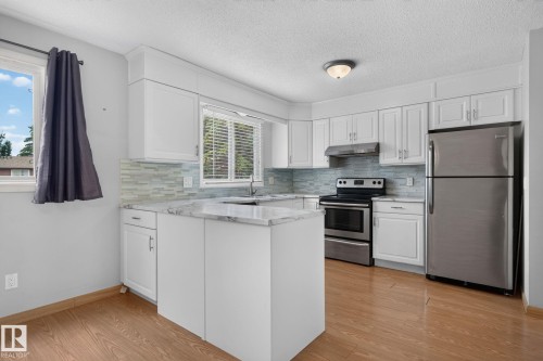 Kitchen featuring white cabinetry, light-toned countertops, a glass tile backsplash, and stainless steel appliances - 10644 158 Avenue Nw, Edmonton, AB - Indoor Photo Showing Kitchen With Stainless Steel Kitchen