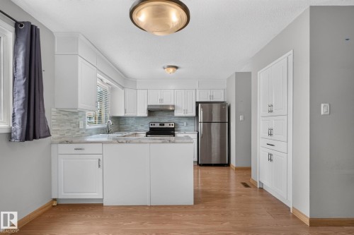 Modern kitchen featuring white cabinetry, light-toned countertops, a full stainless steel appliance suite, and wood-finish flooring - 10644 158 Avenue Nw, Edmonton, AB - Indoor Photo Showing Kitchen