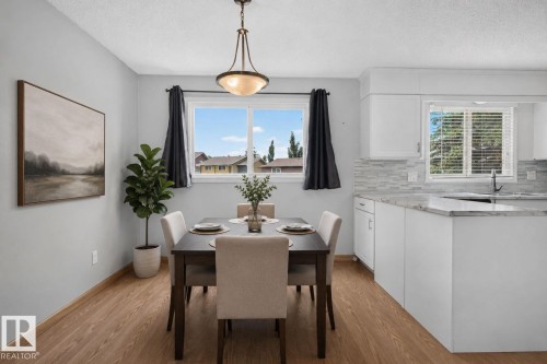 Open-concept dining area with wood-finish flooring, a contemporary chandelier, and a large window - 10644 158 Avenue Nw, Edmonton, AB - Indoor Photo Showing Dining Room