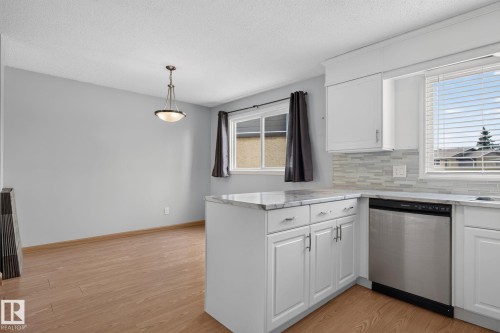 Kitchen featuring white cabinetry, light-toned countertops, a light tile backsplash, and a stainless steel dishwasher - 10644 158 Avenue Nw, Edmonton, AB - Indoor Photo Showing Kitchen With Stainless Steel Kitchen