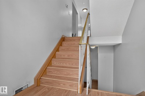 Multi-level staircase featuring wood-finish treads and risers, a wood-finish handrail, white painted balusters, and a contemporary flush-mount ceiling light - 10644 158 Avenue Nw, Edmonton, AB - Indoor Photo Showing Other Room