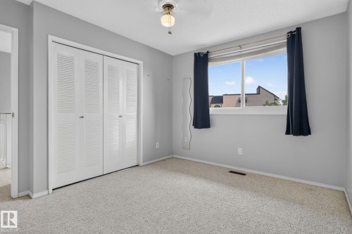 Bedroom featuring light gray wall paint, textured carpeting, and a window with a building backdrop - 10644 158 Avenue Nw, Edmonton, AB - Indoor