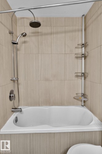 Bathtub with light-toned wall tile surround, shower/tub combination faucet, and a wall-mounted showerhead - 10644 158 Avenue Nw, Edmonton, AB - Indoor Photo Showing Bathroom