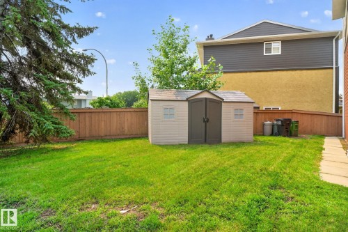 Expansive green lawn featuring a storage shed with double doors, perimeter wood fencing, and a concrete pathway - 10644 158 Avenue Nw, Edmonton, AB - Outdoor With Exterior