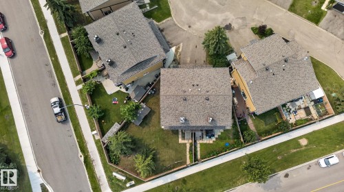 Residential property featuring a shingled roof, attached outdoor deck, fenced backyard with mature trees, and a concrete driveway - 10644 158 Avenue Nw, Edmonton, AB - Outdoor