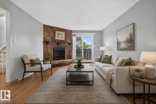 Living area featuring a stone-clad fireplace with a built-in mantel, wood-finish flooring, and a sliding glass door opening to an exterior balcony - 10644 158 Avenue Nw, Edmonton, AB - Indoor Photo Showing Living Room With Fireplace