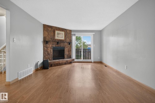 Living space featuring wood-finish flooring, a stone-clad fireplace with a hearth, and a sliding glass door providing exterior access - 10644 158 Avenue Nw, Edmonton, AB - Indoor Photo Showing Living Room With Fireplace