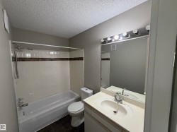 Bathtub with a shower fixture, mosaic tile accent, single vanity with an integrated sink, and a large mirror with overhead lighting - 