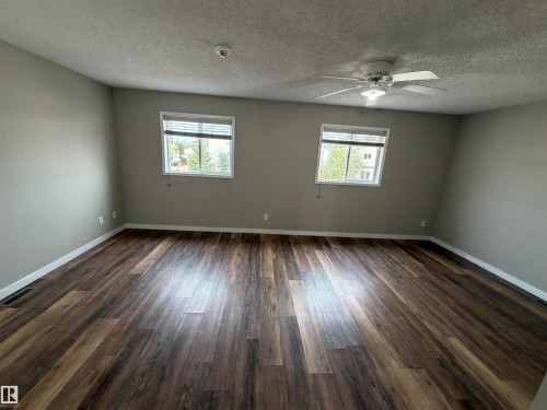 Spacious room featuring wood-finish flooring, neutral wall paint, two windows with blinds, and a ceiling fan with integrated lighting - 1535 80A Street Nw, Edmonton, AB - Indoor Photo Showing Other Room