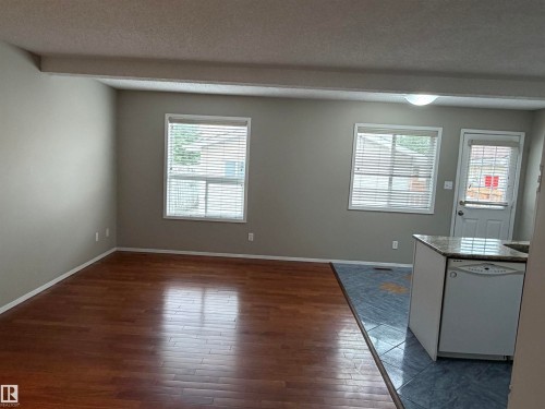 Wood-finish flooring, two windows with blinds, light gray wall paint, kitchen island with granite-style countertop, and a built-in dishwasher - 1535 80A Street Nw, Edmonton, AB - Indoor Photo Showing Other Room