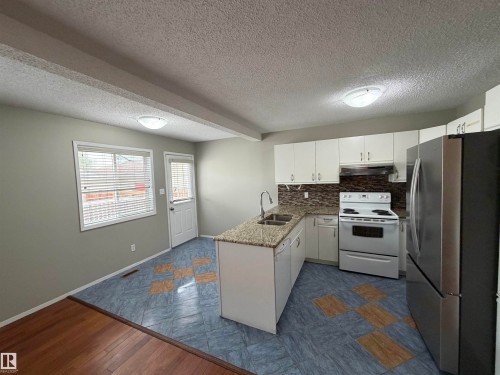 Kitchen featuring white cabinetry, a central island with dual sinks, granite-look countertops, and a mosaic tile backsplash - 1535 80A Street Nw, Edmonton, AB - Indoor Photo Showing Kitchen With Double Sink