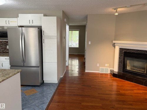 Hardwood-style flooring, corner fireplace with a tiled surround, built-in white cabinetry, and a stone-look countertop - 1535 80A Street Nw, Edmonton, AB - Indoor With Fireplace