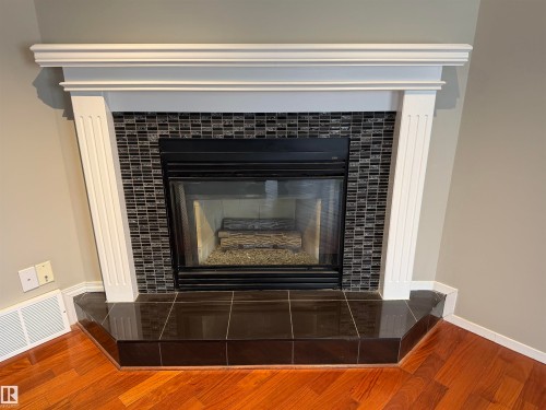Fireplace with a white wood mantel, dark mosaic tile surround, and a dark tile hearth - 1535 80A Street Nw, Edmonton, AB - Indoor Photo Showing Living Room With Fireplace