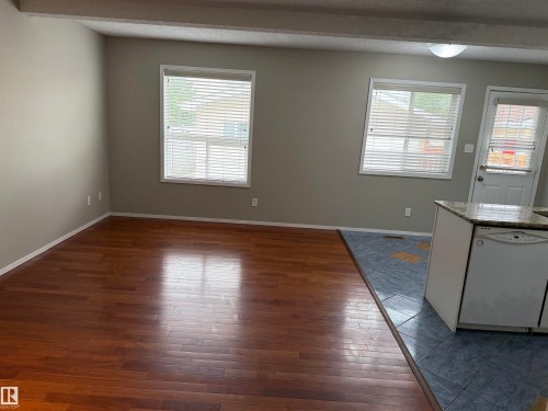 Hardwood-finish flooring, light grey wall paint, two windows with blinds, a white exterior door, and a kitchen island with a granite-style countertop - 1535 80A Street Nw, Edmonton, AB - Indoor Photo Showing Other Room