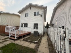 Rear exterior featuring a two-story design with white siding, a full-width deck with white railings, and a concrete paver patio - 