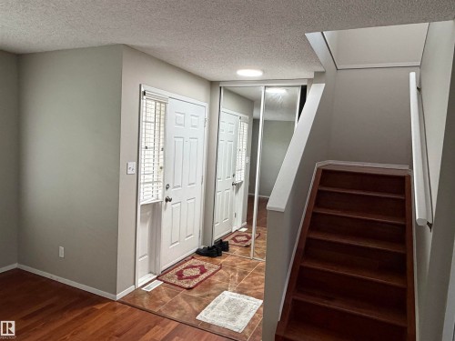 Entryway featuring wood-finish flooring, a white paneled door with blinds, and mirrored sliding closet doors - 1535 80A Street Nw, Edmonton, AB - Indoor Photo Showing Other Room