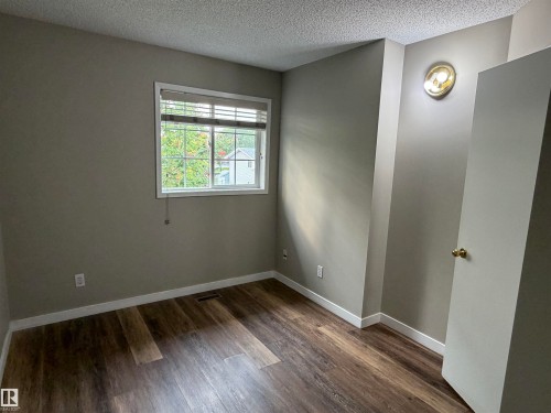 Wood-finish flooring, neutral wall paint, white trim, and a window with blinds - 1535 80A Street Nw, Edmonton, AB - Indoor Photo Showing Other Room