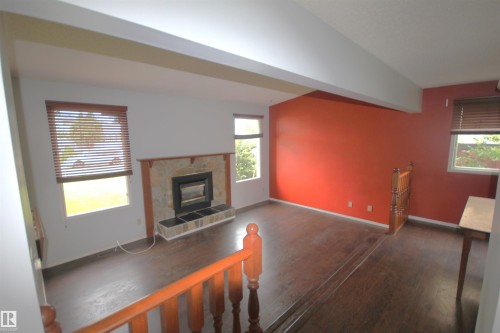 Wood-finish flooring, stone-faced fireplace with hearth, multiple windows with blinds, and a wood railing with balusters - 16547 113 Street Nw, Edmonton, AB - Indoor With Fireplace
