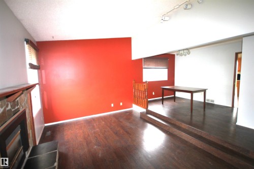 Wood-finish flooring throughout, stone-clad fireplace, and track lighting fixture - 16547 113 Street Nw, Edmonton, AB - Indoor Photo Showing Other Room With Fireplace