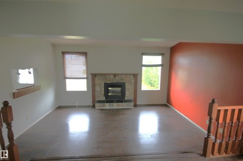 Stone-clad fireplace with hearth, wood-finish flooring, two windows, and a wood railing - 16547 113 Street Nw, Edmonton, AB - Indoor Photo Showing Living Room With Fireplace