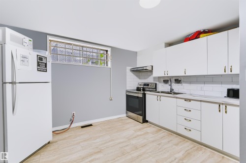White cabinetry with gold-finish hardware, stainless steel range with overhead hood, white subway tile backsplash, and light wood-finish flooring - 8723 81 Avenue Nw, Edmonton, AB - Indoor Photo Showing Kitchen With Double Sink