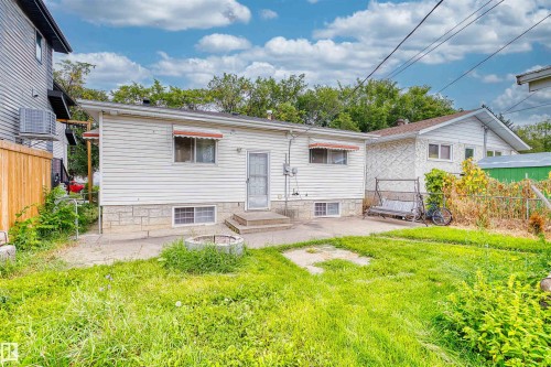Rear exterior with white siding, stone foundation, concrete patio, and a fire pit - 8723 81 Avenue Nw, Edmonton, AB - Outdoor